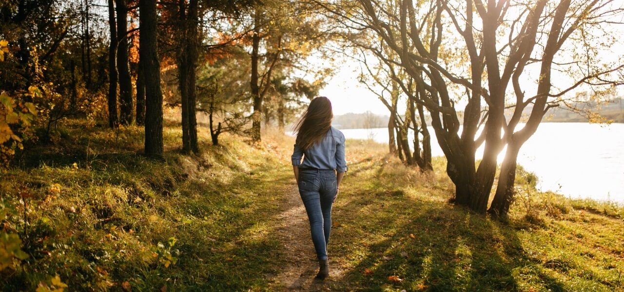 A girl walks through a serene forest, with a lake by her side, taking in the natural beauty as a form of therapy for her mind and soul.