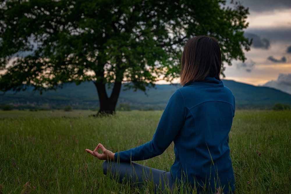 A woman sits cross-legged in a lush green field in deep meditation