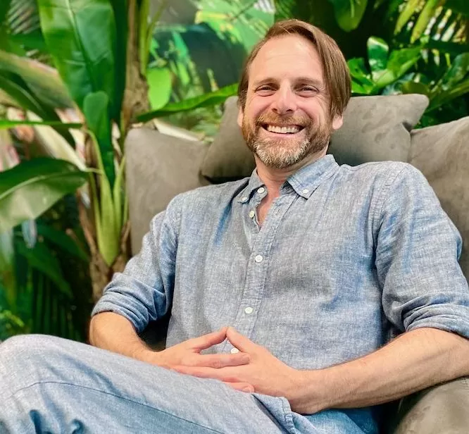 Joel Myers sitting on a couch and smiling